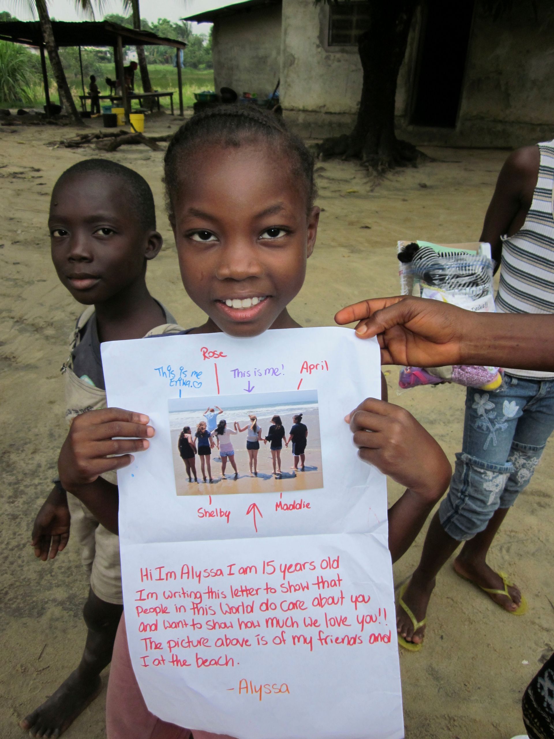 Two children outdoors hold a handwritten poster with a small photo collage.