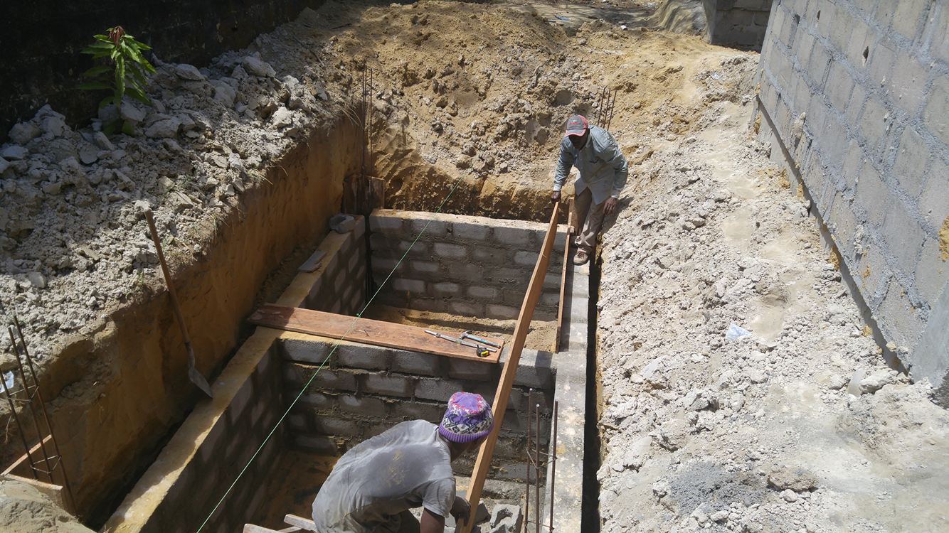 Workers in a deep excavation site, installing wooden supports in an underground trench.