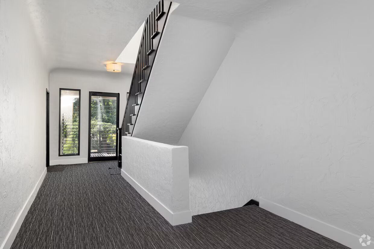 Hallway with stairs and doorway. White walls, grey carpet. Black railing and trim.