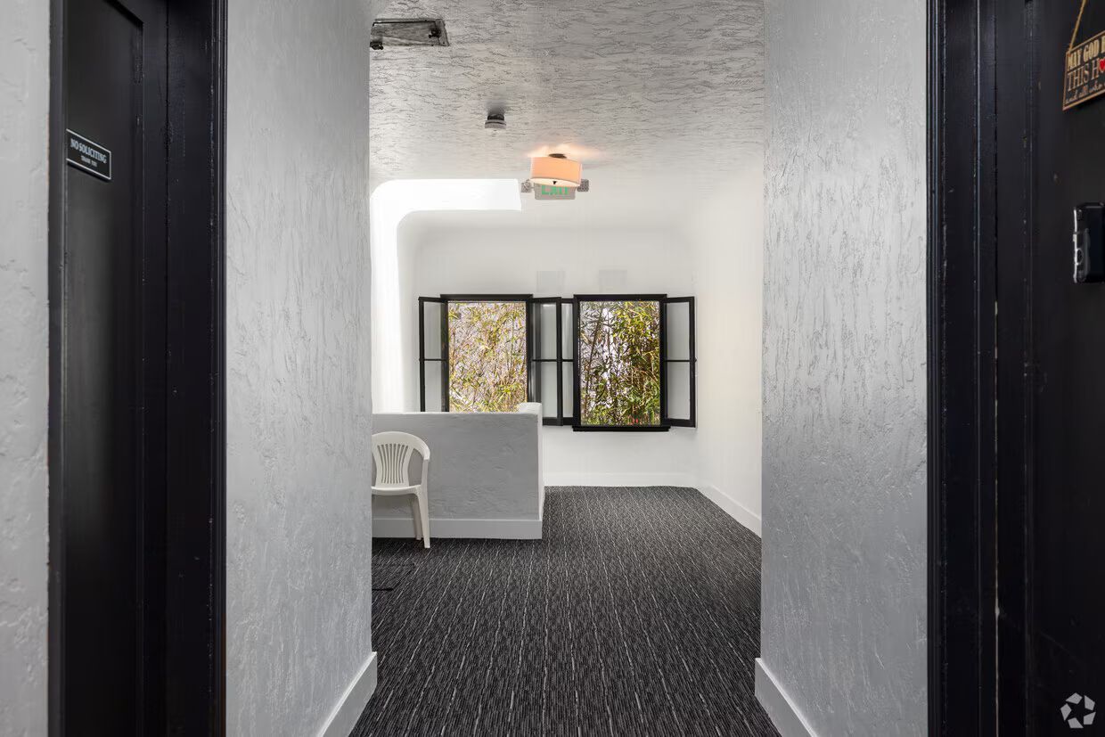 Hallway with dark doors, textured white walls, a reception desk, and two windows.