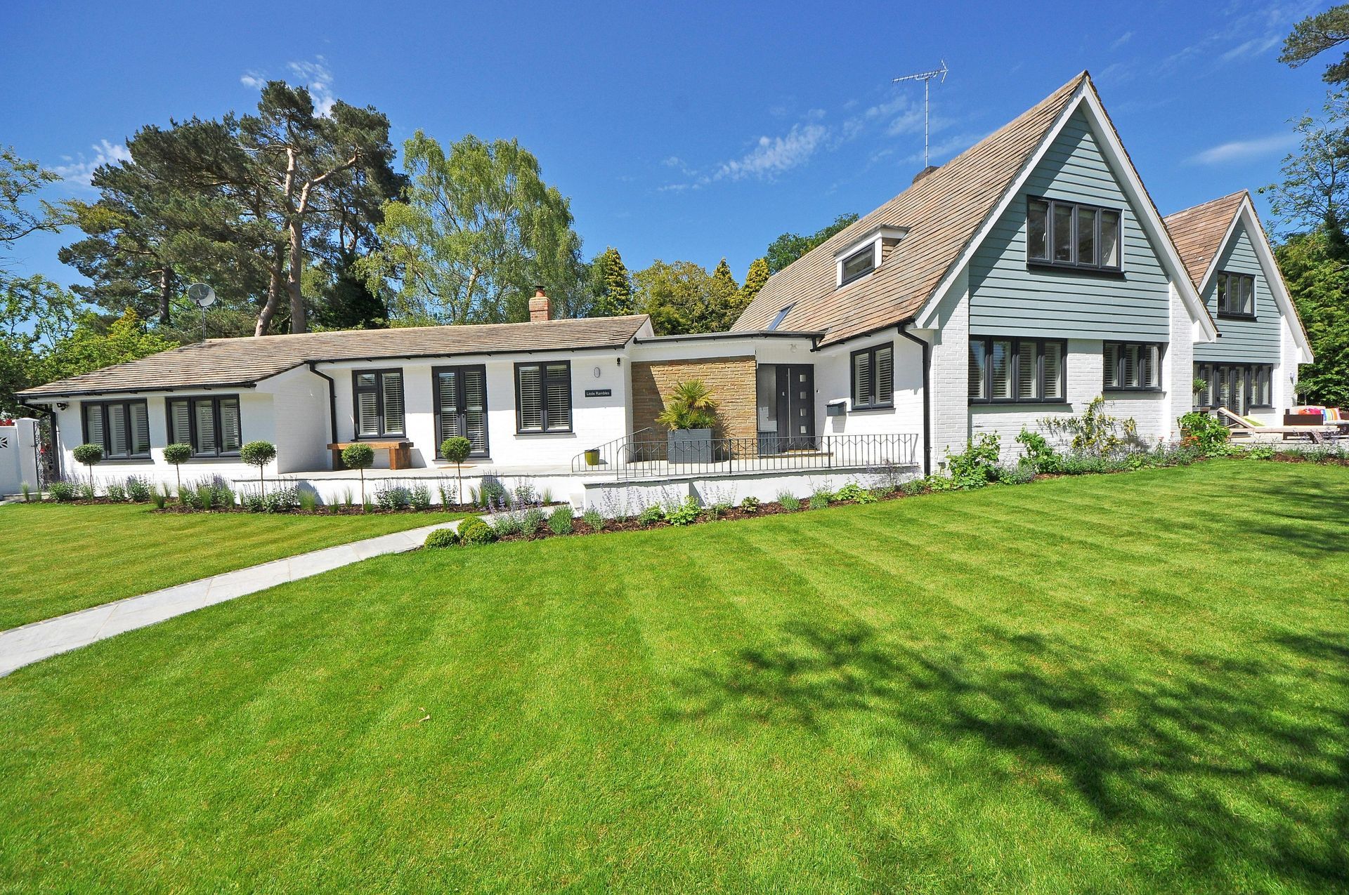 A white house with gray siding and a shingled roof, set against a bright blue sky behind a manicured green lawn.