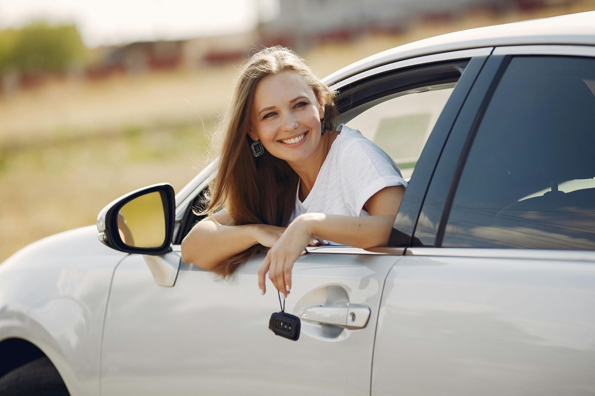 Woman smiling from the driver’s seat of a white car, leaning out the window outdoors