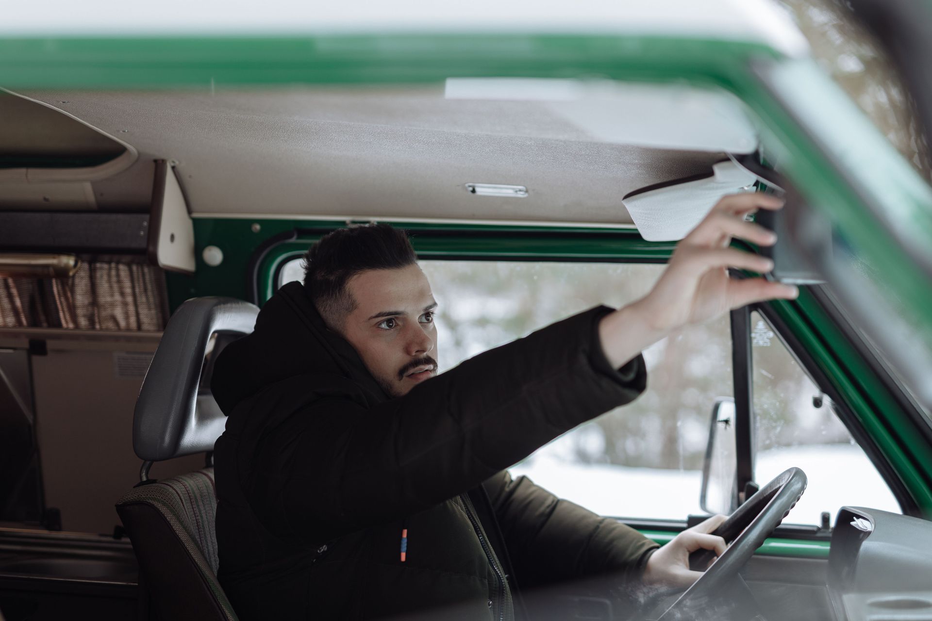 Driver adjusting the rearview mirror before driving, a safe driving habit that earns discounts