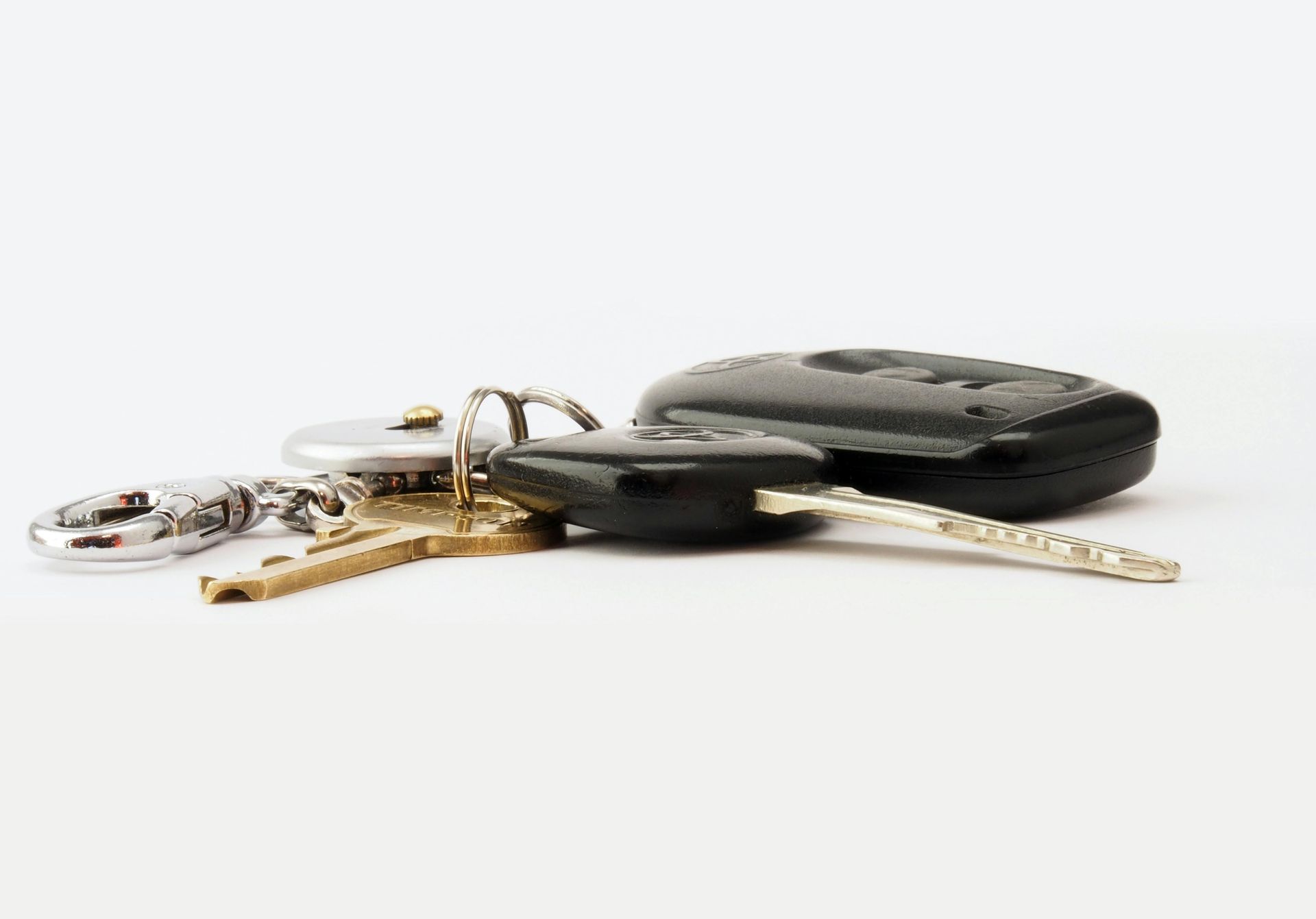 A close-up of a small set of keys, including a brass key and a black car key fob, resting on a plain white surface.