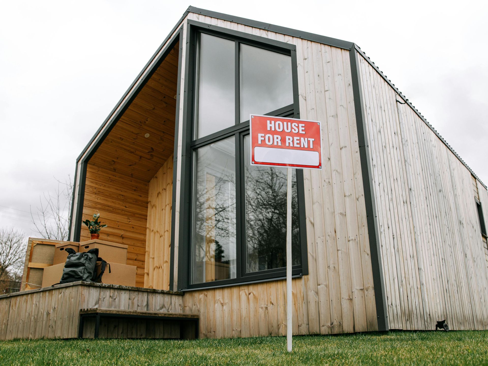 A modern, light-wood tiny house with large windows sits on a grassy lawn with a 