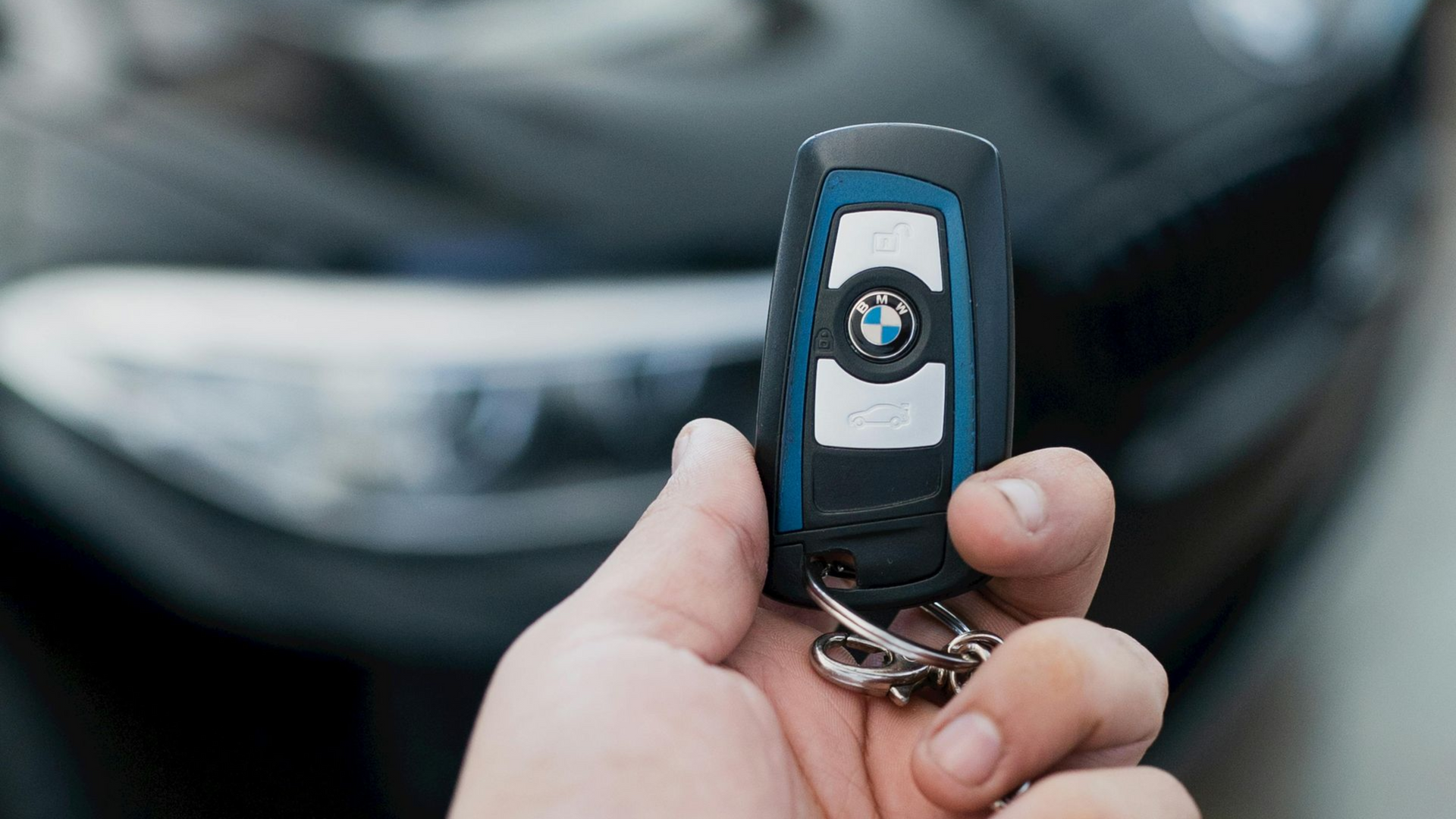 A hand holds a black and blue BMW car key fob against the blurred background of a dark car.