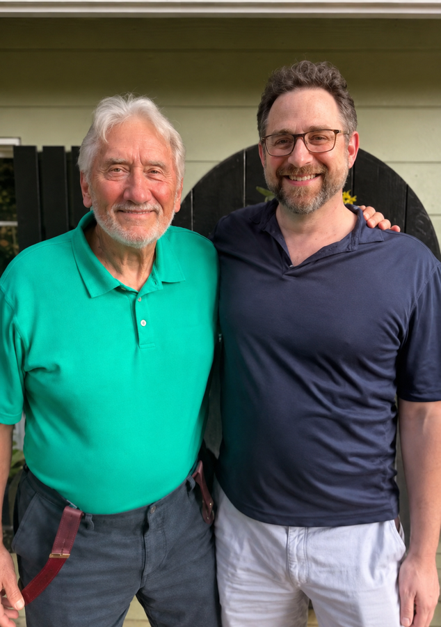 Two men standing close together, smiling outdoors; one in a green polo, the other in a navy shirt.