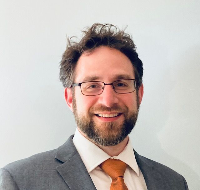 A man wearing glasses and a suit is smiling for the camera.