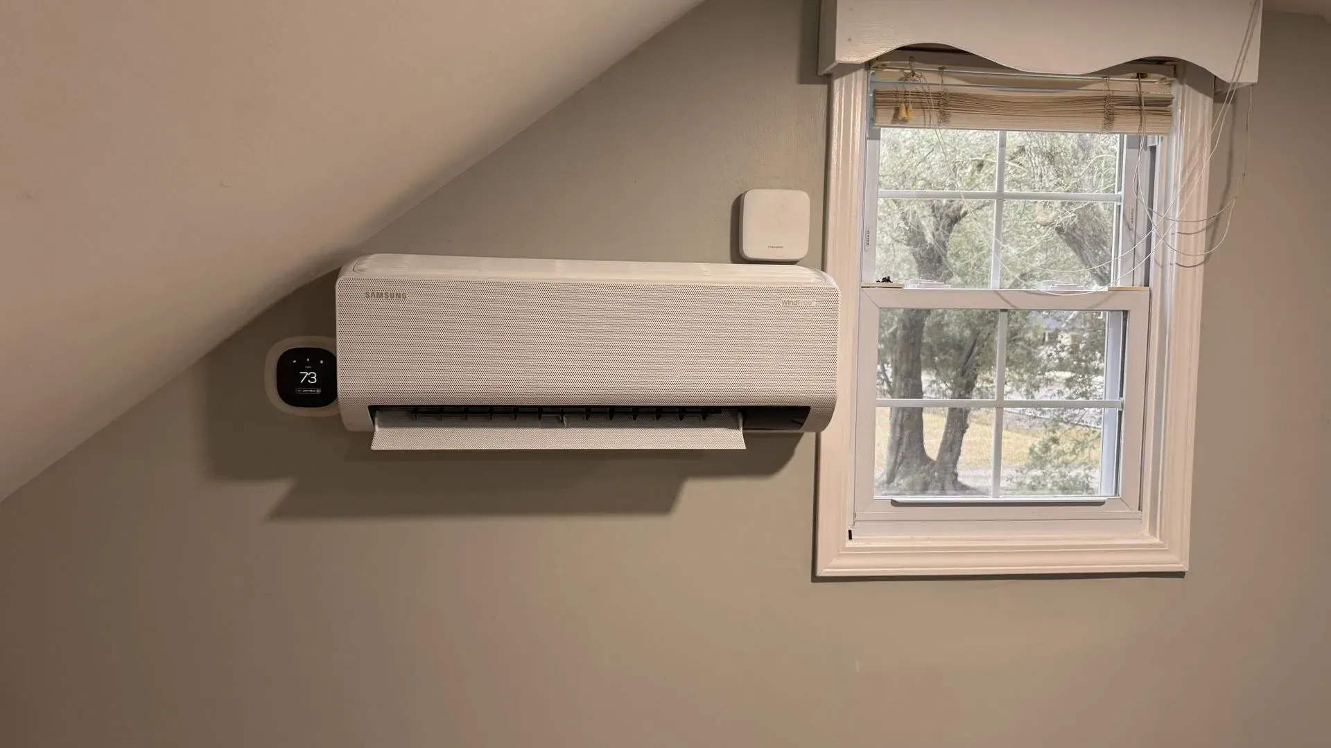 Wall-mounted air conditioner beside a small window in an attic room