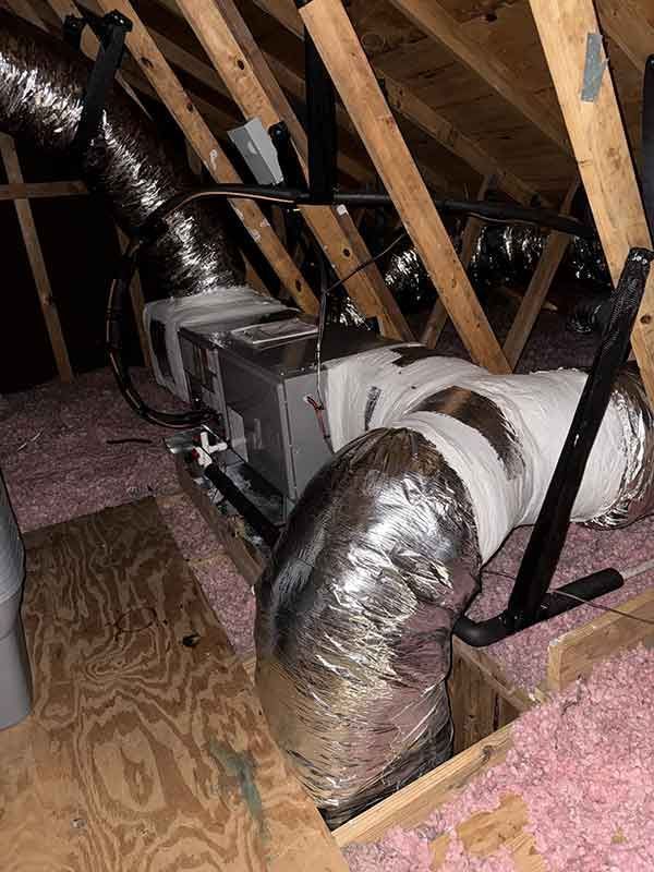 Attic HVAC ductwork and insulated vents beneath wooden rafters, with pink insulation on the floor