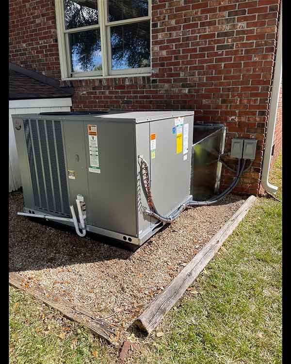 Outdoor HVAC unit beside a brick house wall, with gravel pad and grass nearby