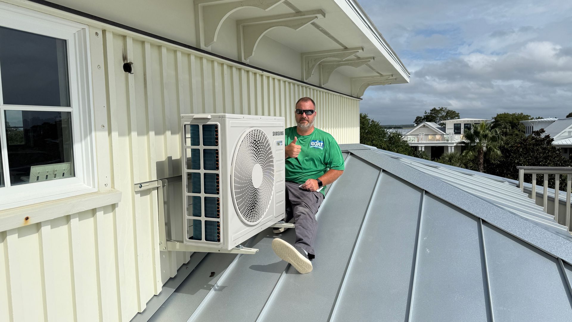 Person on a rooftop beside an air conditioner unit, next to a metal roof and white building exterior