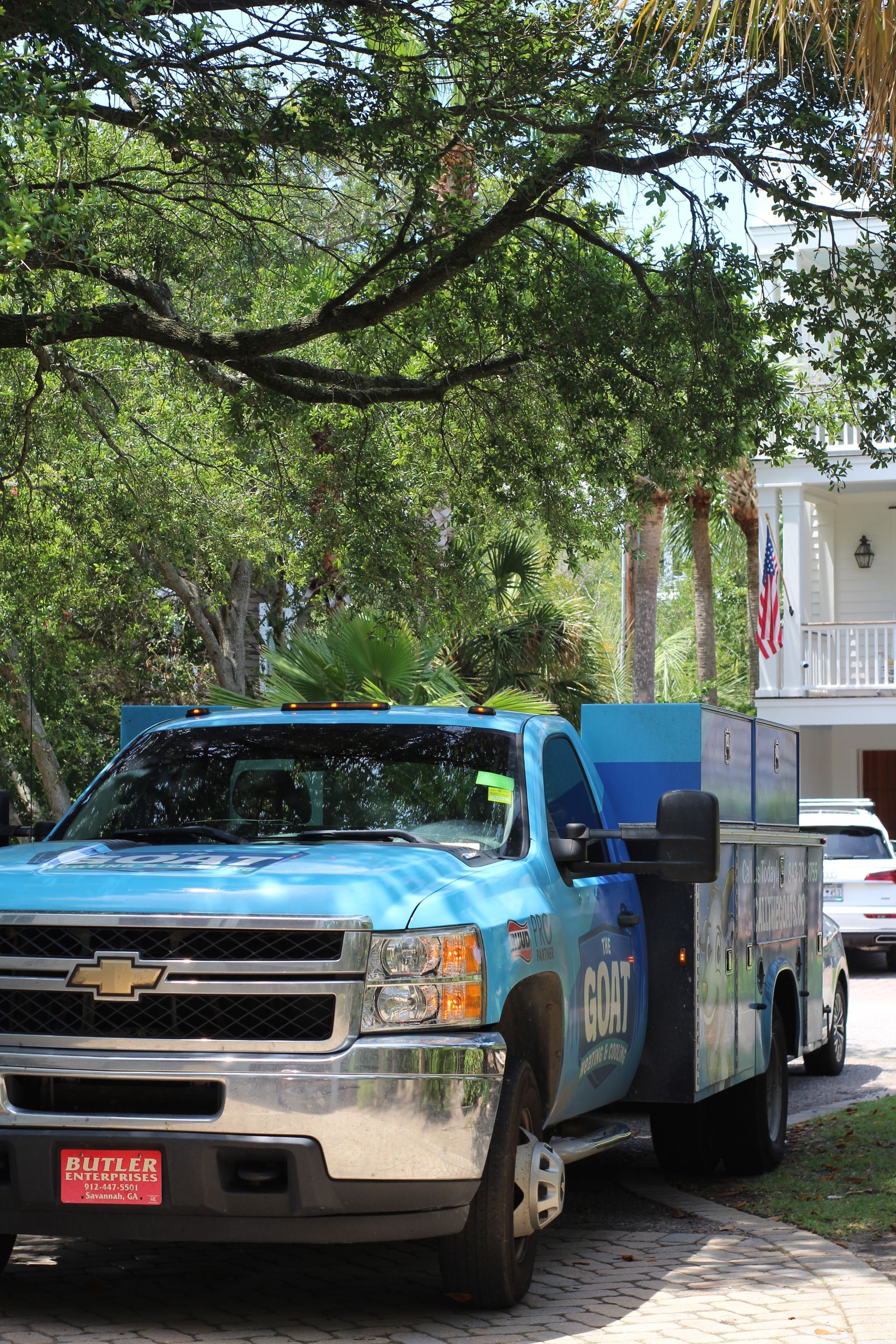 Blue utility truck parked under trees beside a white house