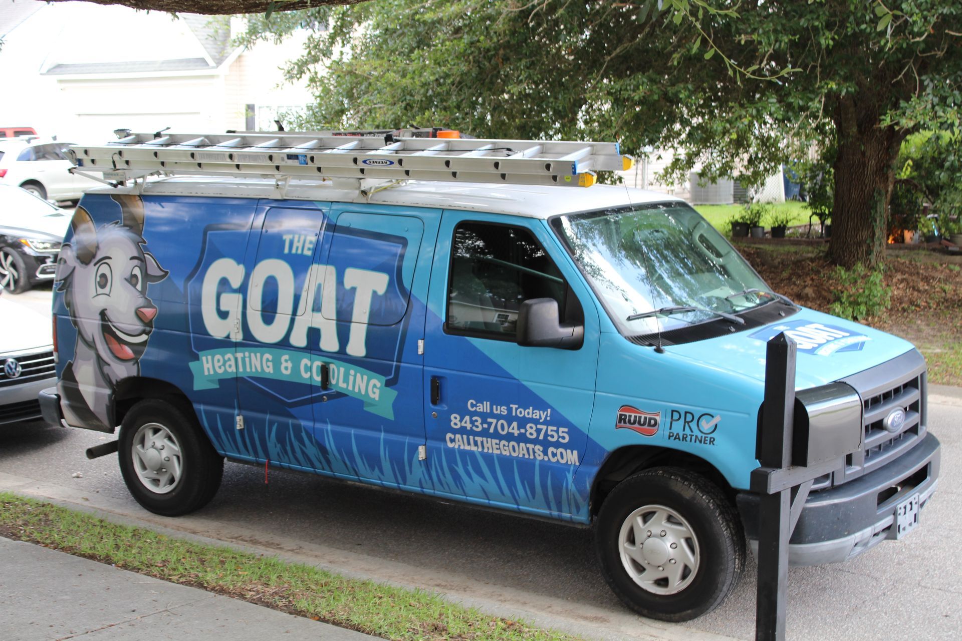 Blue “The GOAT” service van with ladder parked on a residential street