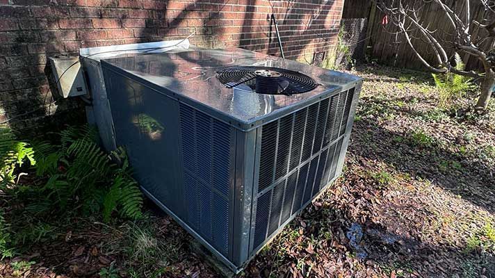 Outdoor HVAC unit beside a brick wall, with a dark metal casing and a fan on top.