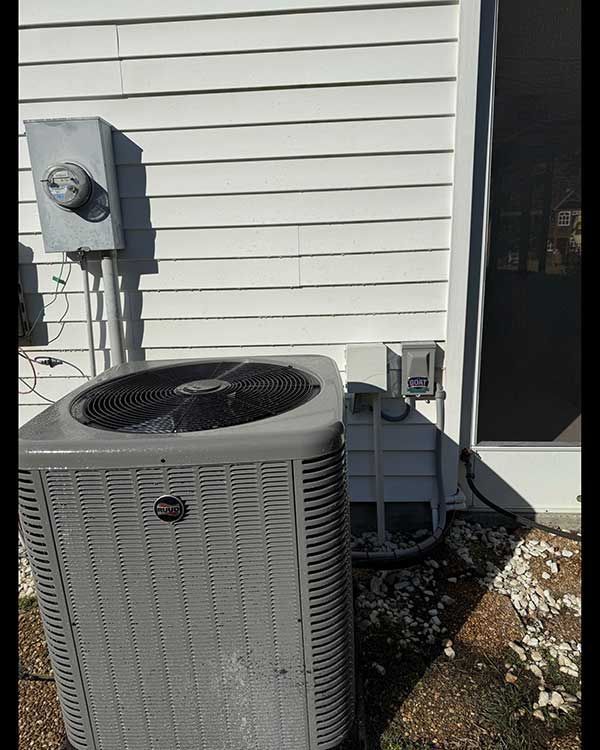 Outdoor air conditioner unit beside a house wall and electrical meter box in bright sunlight