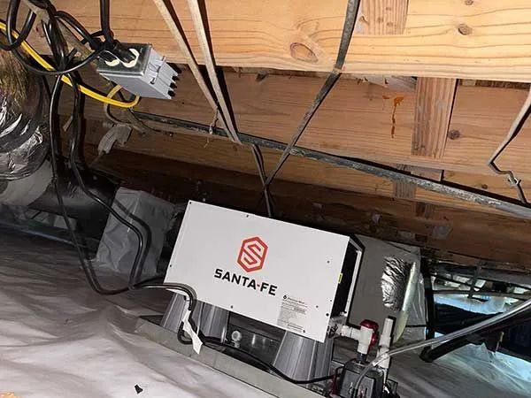 White Santa Fe dehumidifier in a crawlspace under exposed floor joists and wiring.