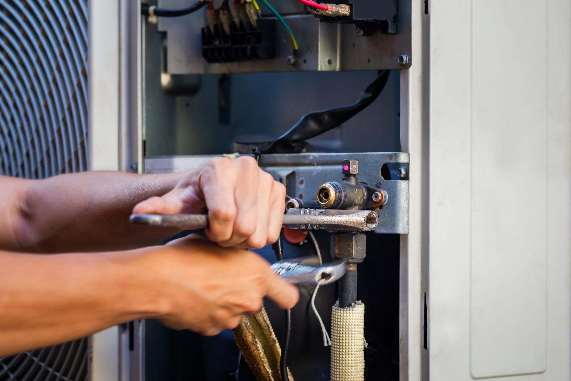 Hands using tools to repair electrical wiring inside an open wall panel.