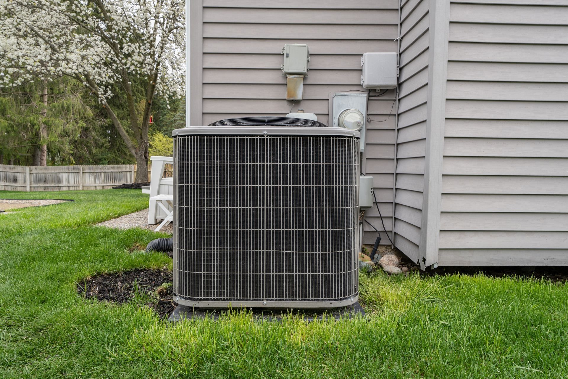 Outdoor air conditioner unit beside a house with gray siding on a grassy lawn.