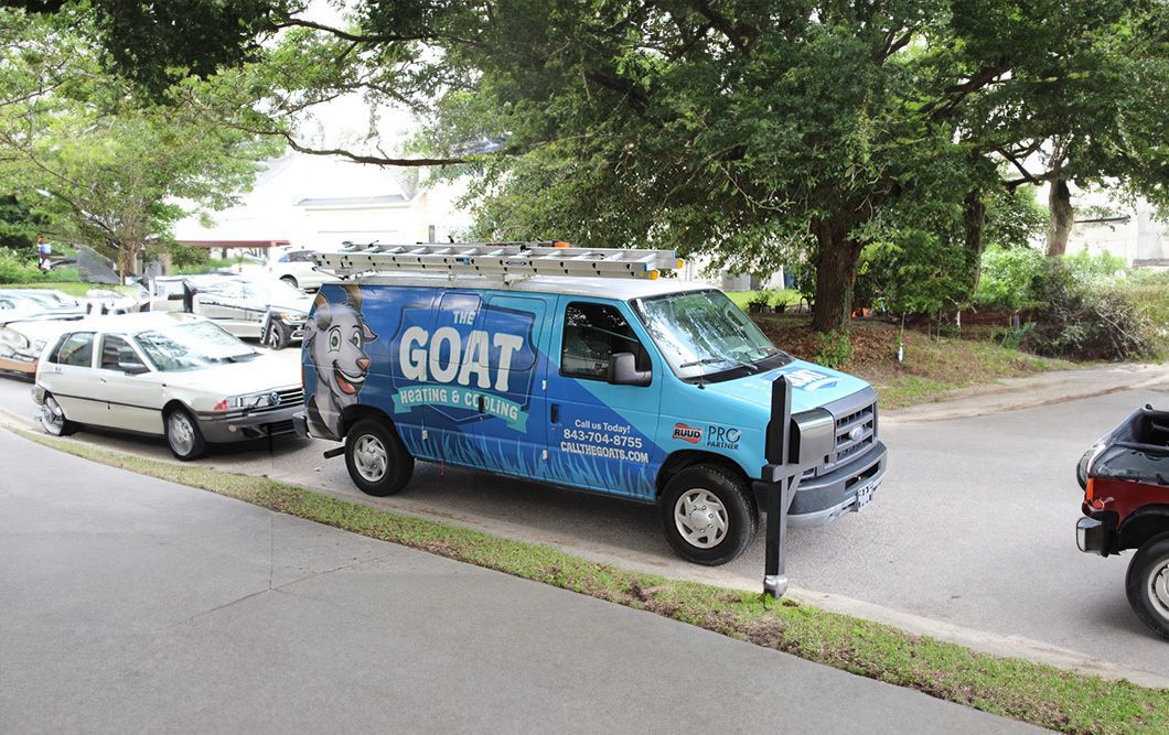 Blue GOAT delivery van parked on a tree-lined street beside a white car