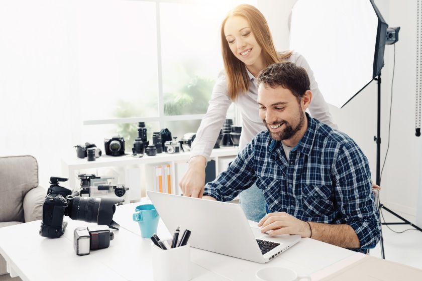 A man and a woman in a studio surrounded by cameras are looking at a laptop