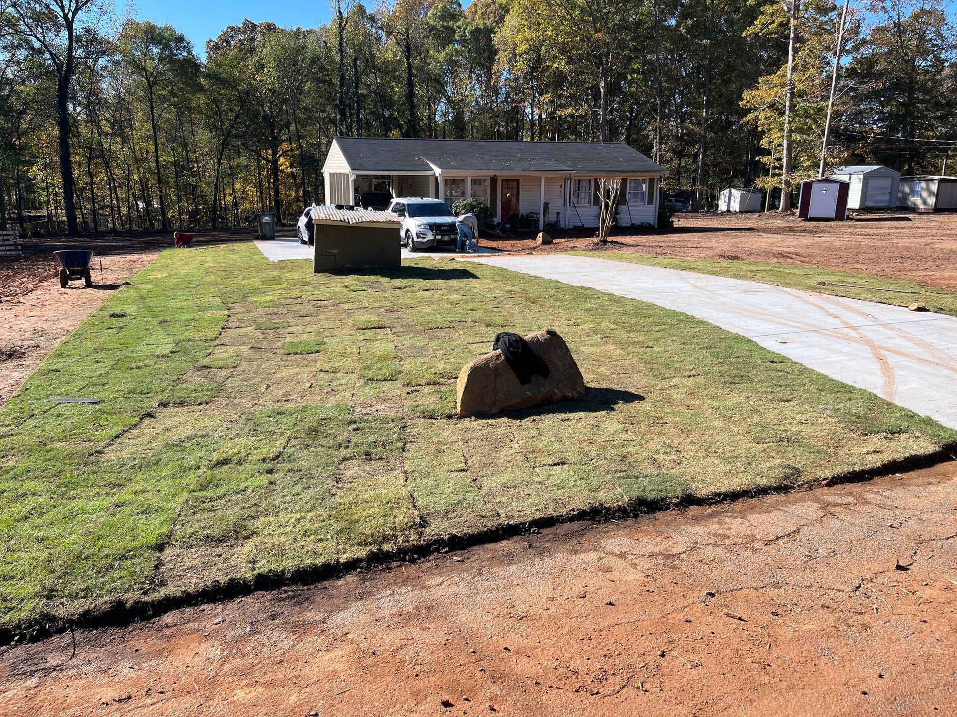 A small house with a freshly sodded lawn and a long driveway on a sunny day.