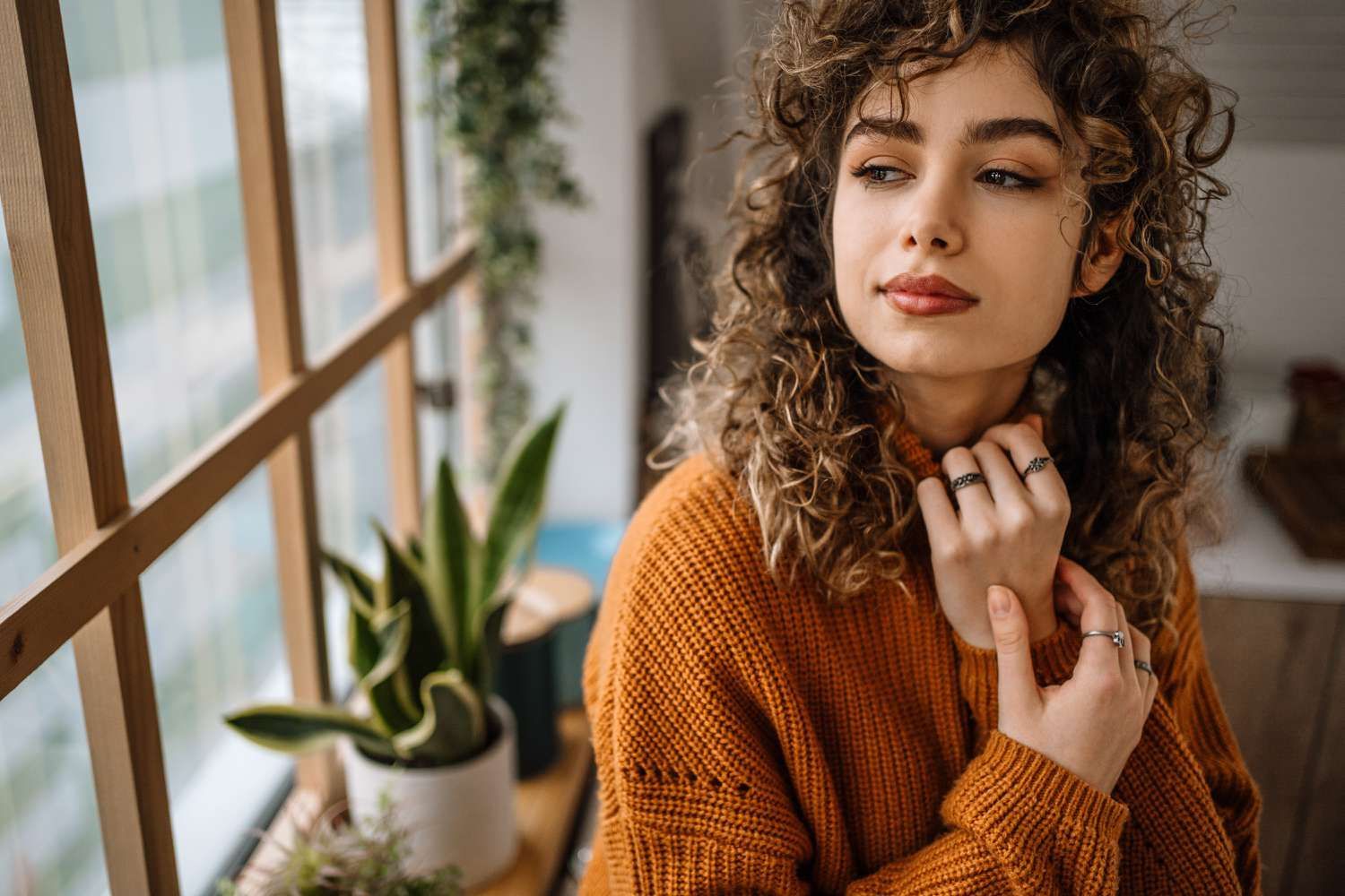 A woman with curly hair is standing in front of a window.