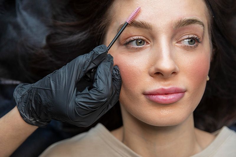 A woman is getting her eyebrows done by a makeup artist.