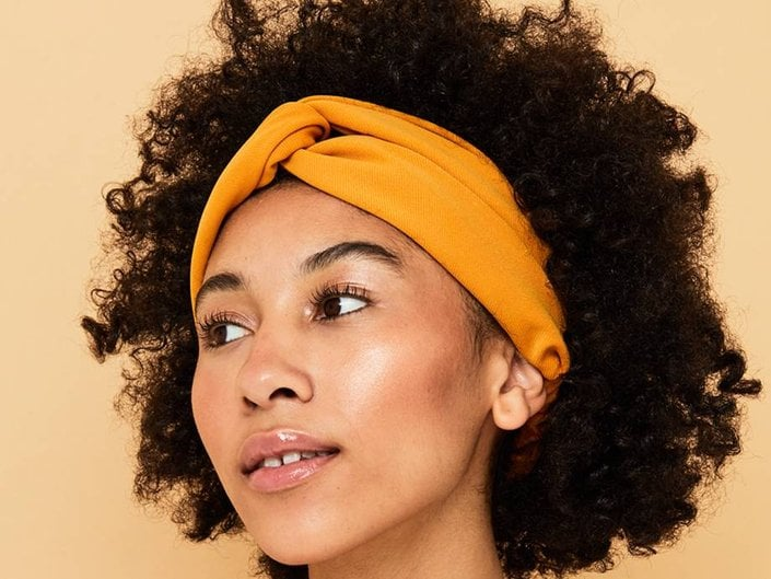A woman with curly hair is wearing a yellow headband.