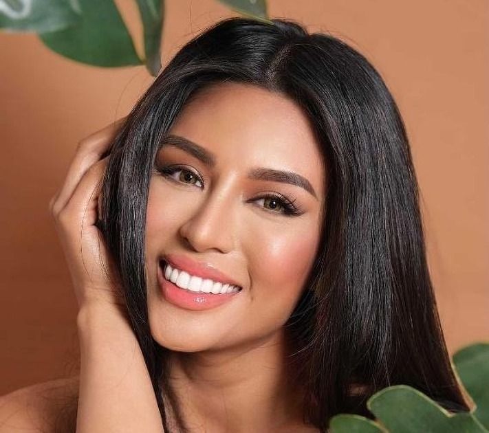 A woman with long black hair is smiling and holding her hair.