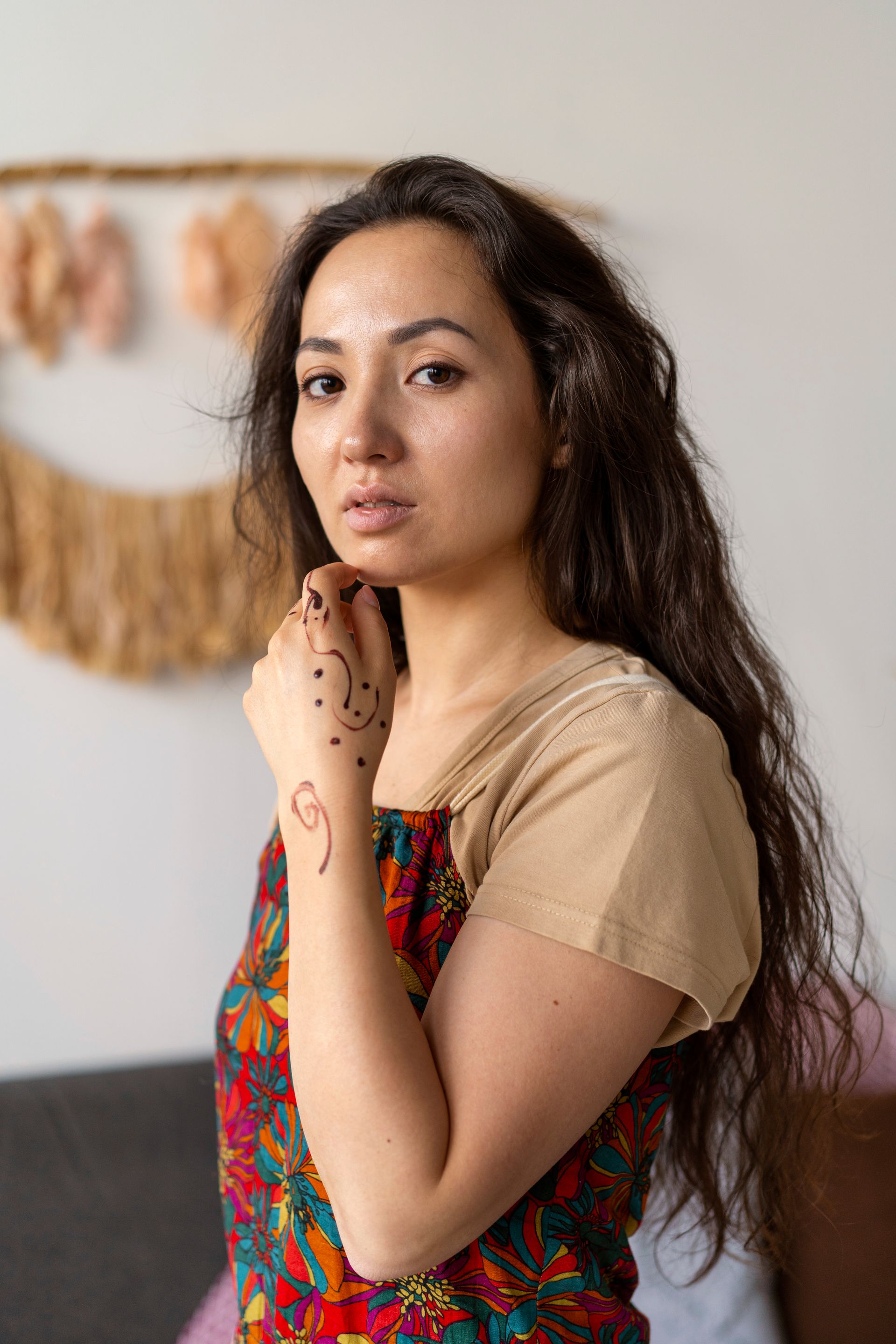 A woman with long hair and a tattoo on her arm is standing in front of a couch.
