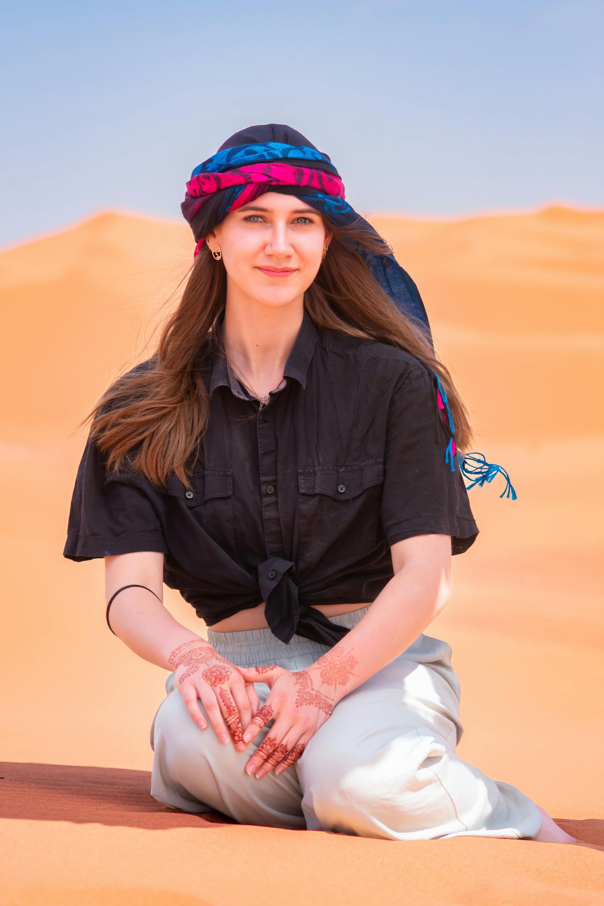 A woman is kneeling down in the desert wearing a turban.