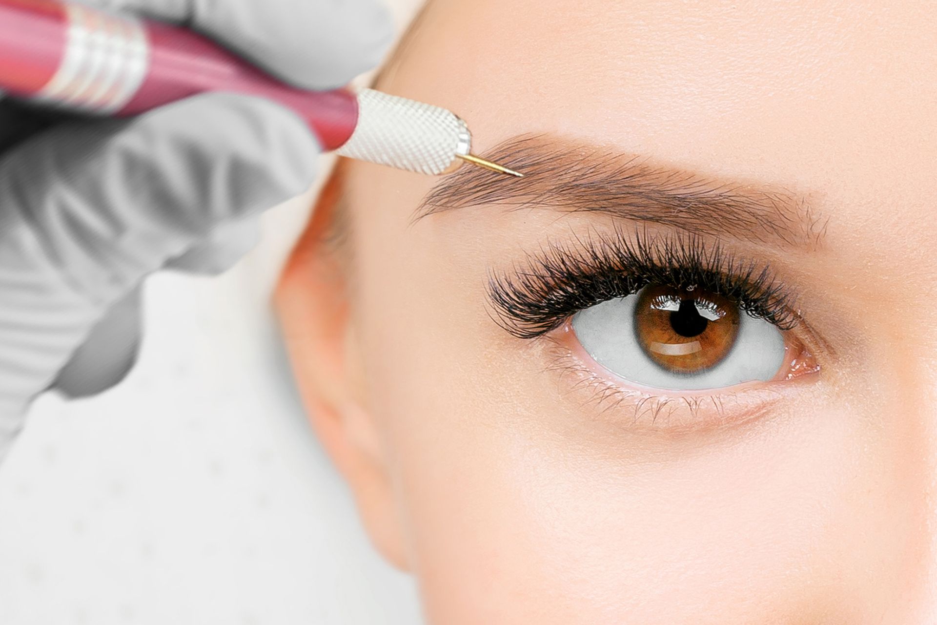 A woman is getting her eyebrows tattooed with a machine.