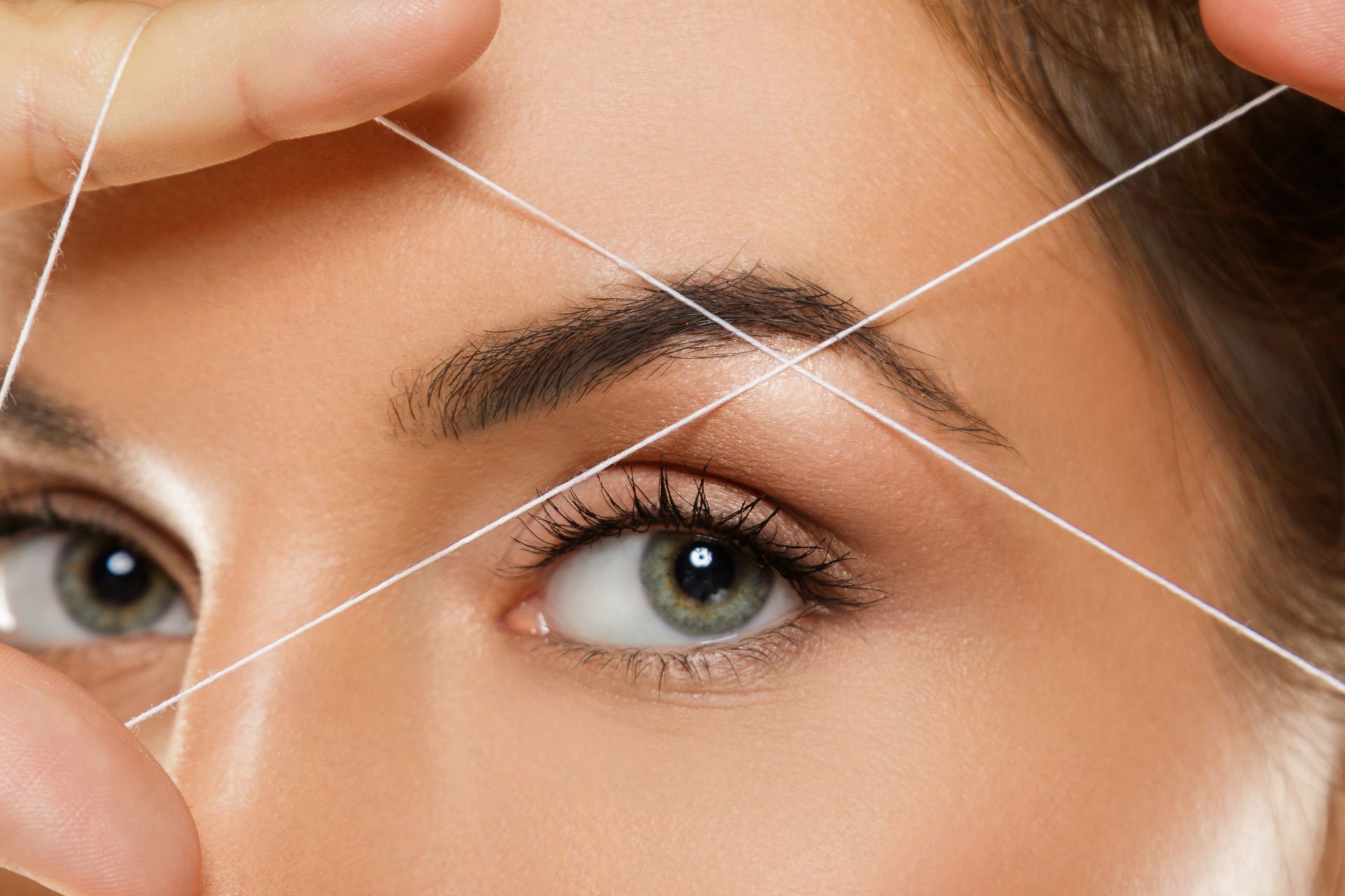 A woman is threading her eyebrows with a string.
