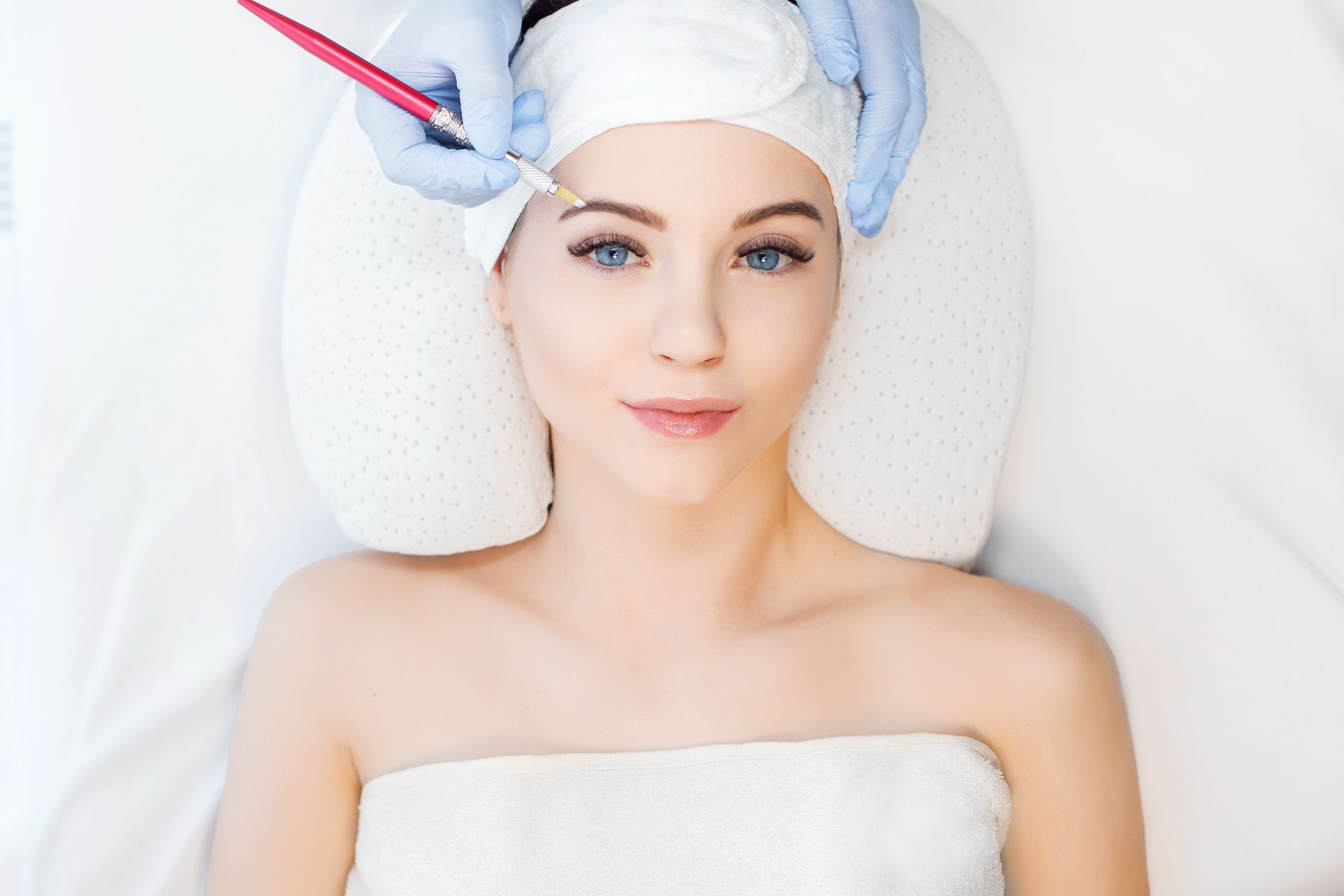 A woman is getting her eyebrows tattooed in a beauty salon.