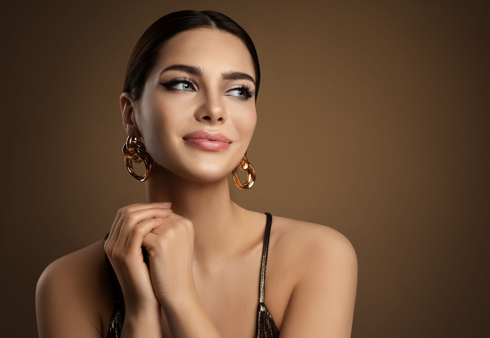 A woman wearing a black top and gold earrings is smiling.