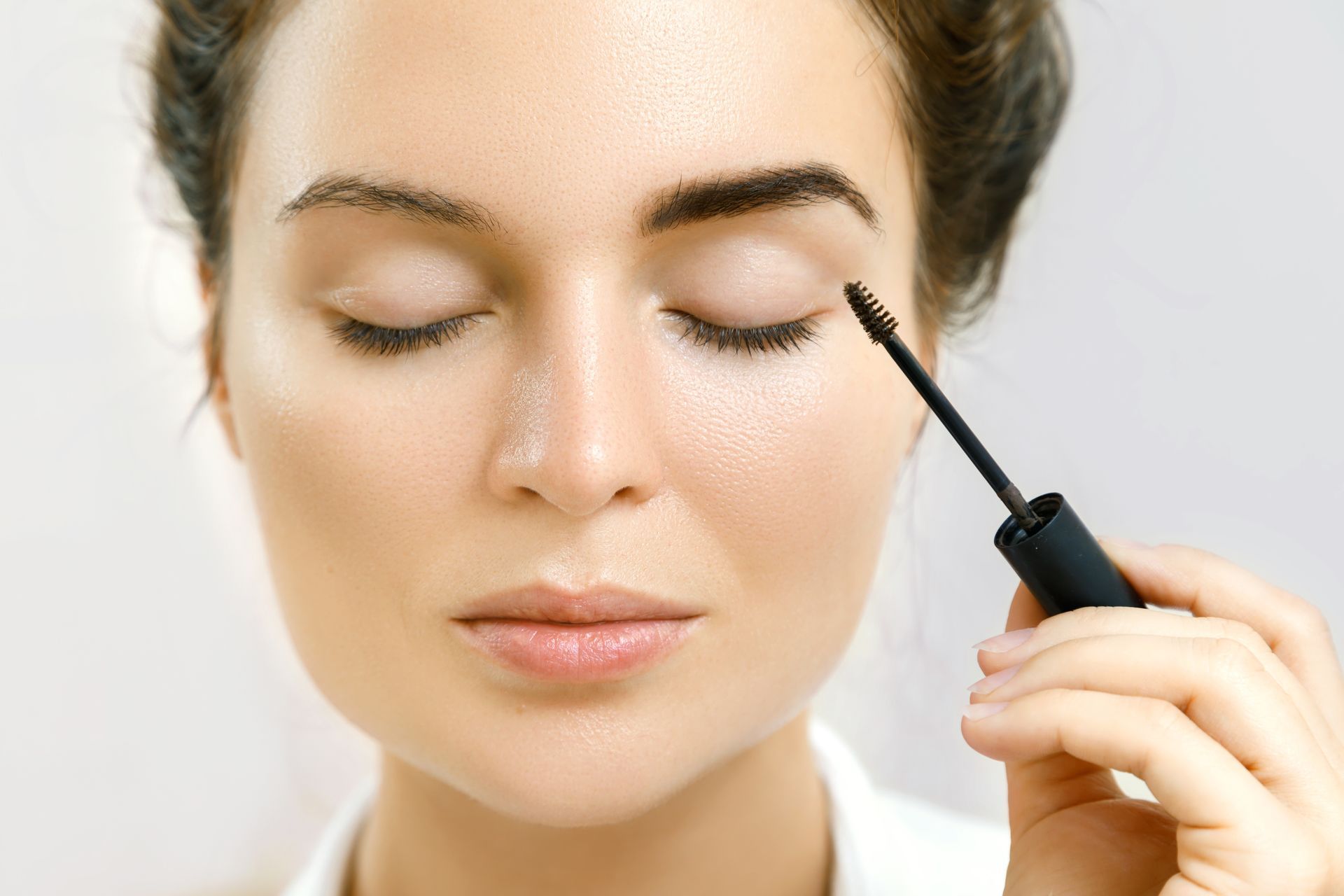 A woman is applying mascara to her eyebrows.