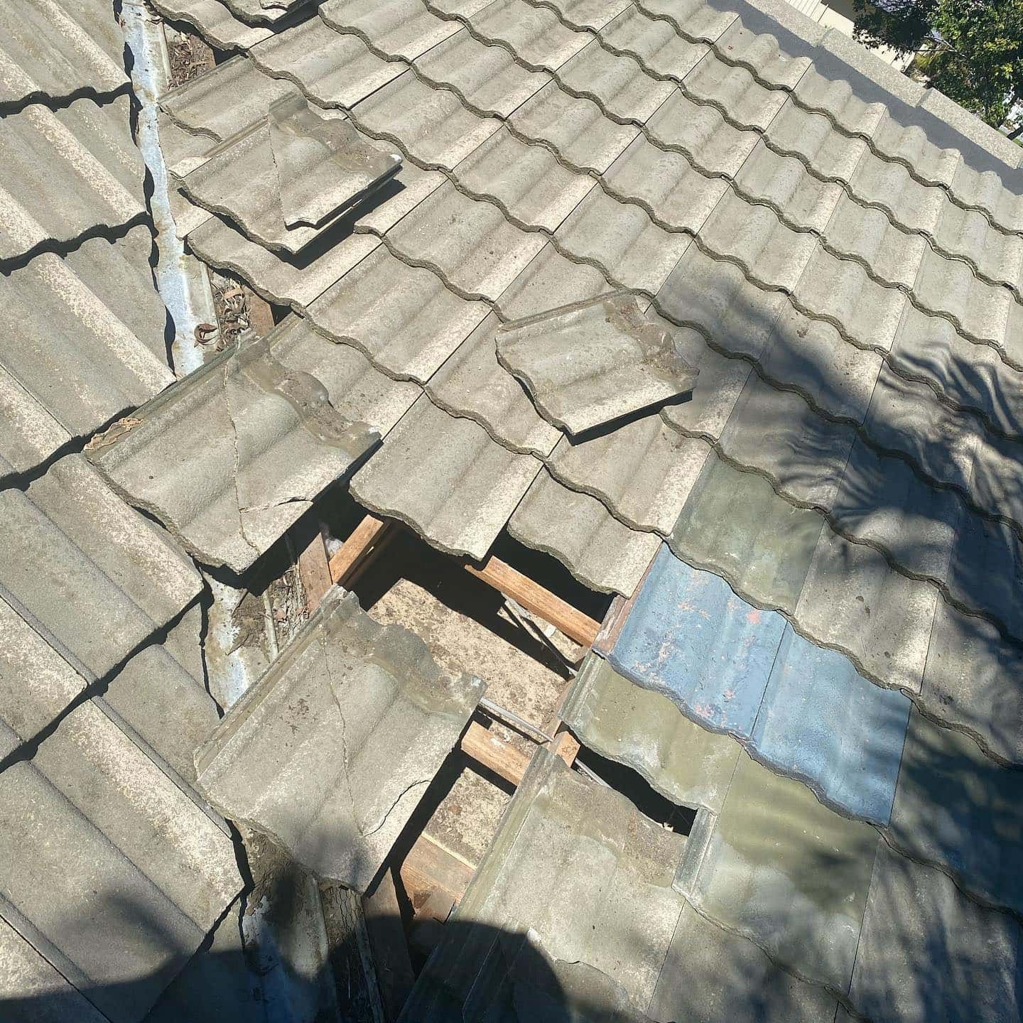 Damaged gray tile roof with missing tiles revealing wooden structure beneath — SEQ Roofing & Painting in Nerang, QLD