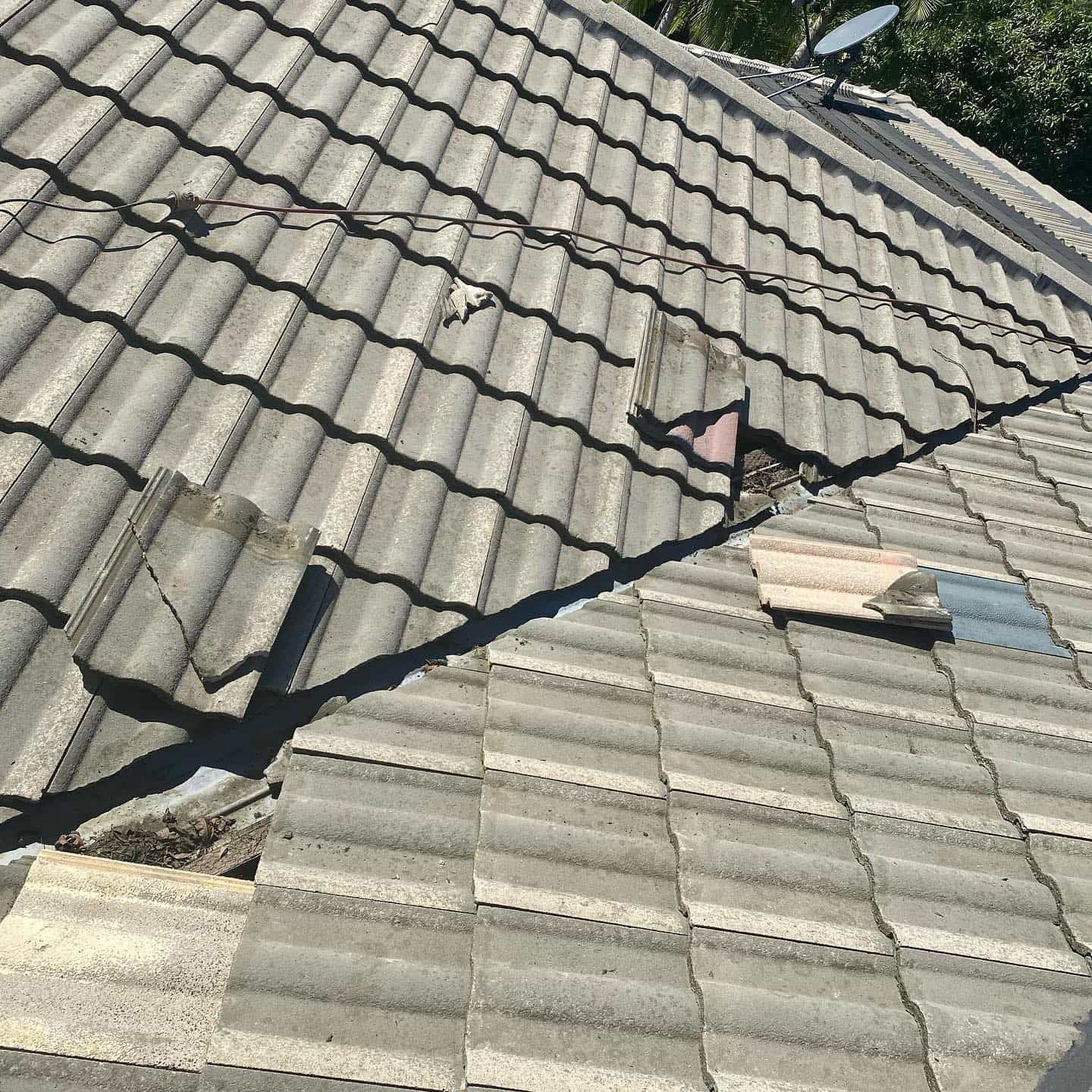 Damaged gray tiled roof with missing and broken tiles, showing a section in need of repair — SEQ Roofing & Painting in Nerang, QLD