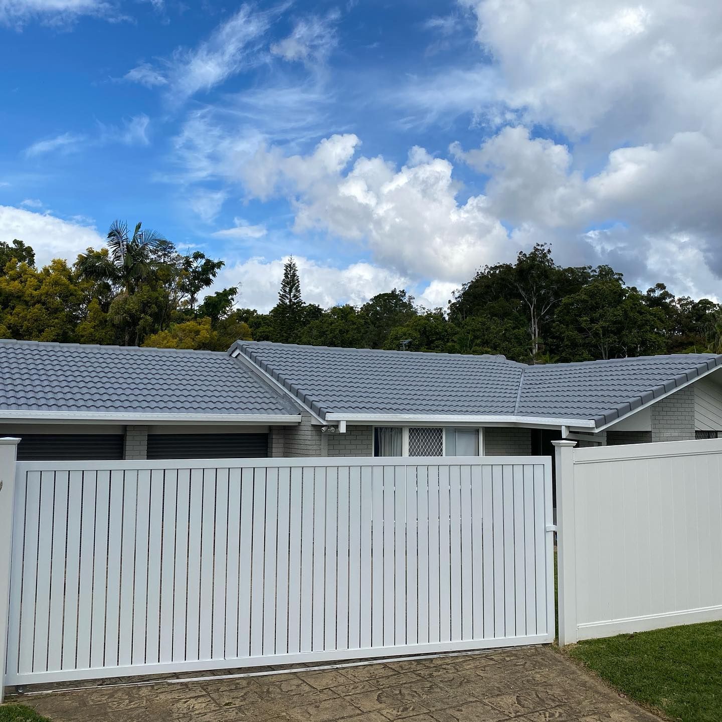 White Fenced House with Blue Roof Under Cloudy Sky — SEQ Roofing & Painting in Coomera, QLD