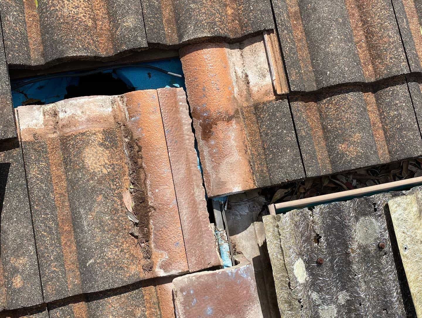 Damaged Terracotta Roof Tiles With a Hole Exposing Blue Underlayment and a Broken Pipe — SEQ Roofing & Painting in Burleigh Heads, QLD