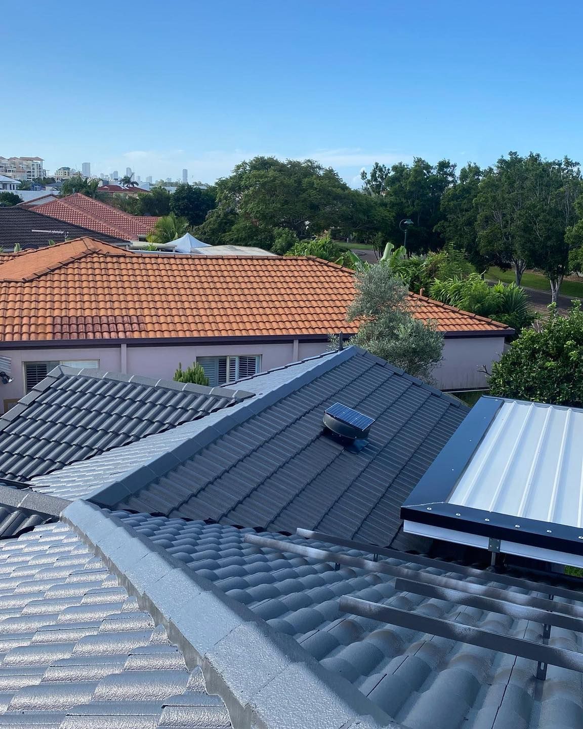 Rooftop view: Dark grey tiled roof with a skylight and metal trim, looking over neighborhood rooftops and trees. — SEQ Roofing & Painting in Nerang, QLD
