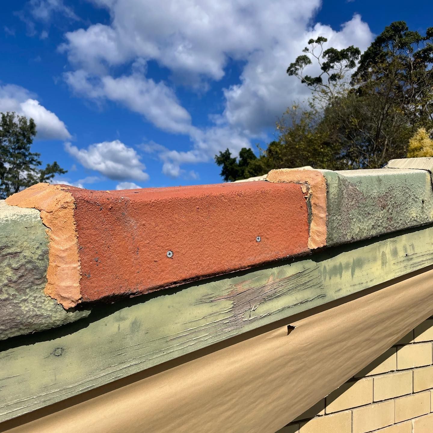 Close-up of a Red Brick Fixed to a Wooden Structure, With Sky and Trees in Background — SEQ Roofing & Painting in Currumbin, QLD