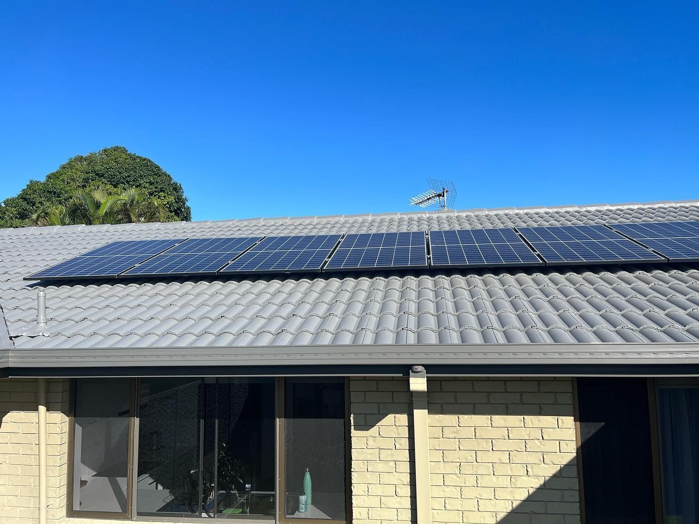 Solar Panels on A Gray Tiled Roof Against a Bright Blue Sky — SEQ Roofing & Painting in Coomera, QLD