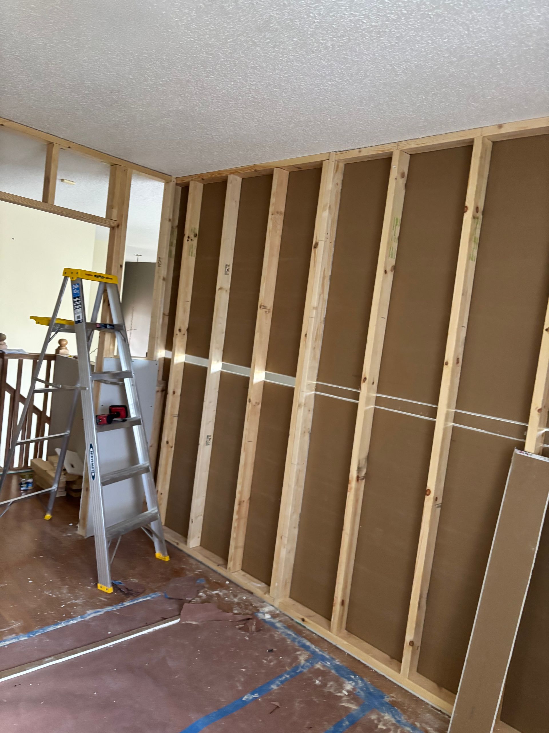 Partially renovated room with exposed wall studs, ladders, and construction materials on the floor