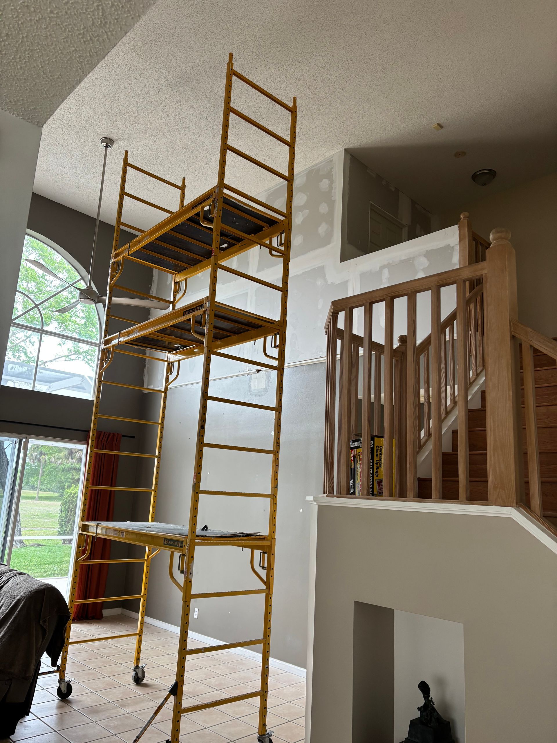Tall yellow scaffold set up in a bright living room beside a staircase and railing.