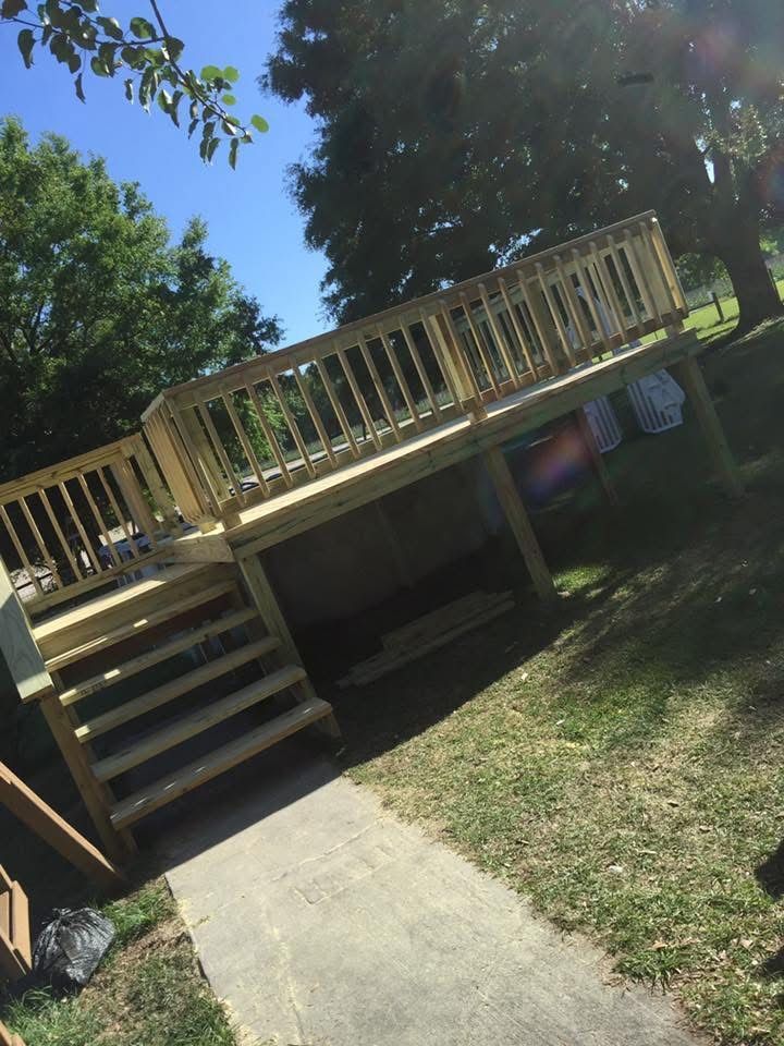 Raised wooden deck with stairs in a sunny backyard beside a concrete path