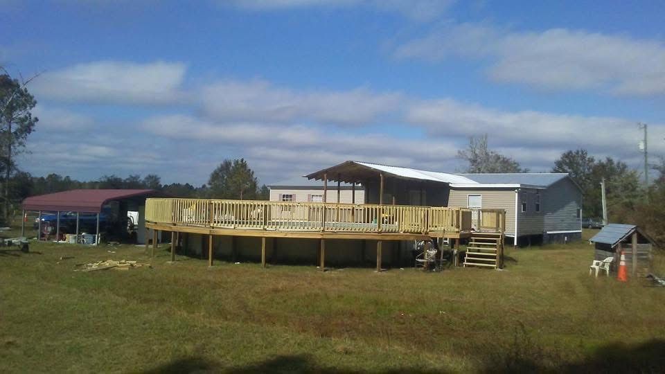 Small house with a wooden deck in a grassy field under a partly cloudy sky.