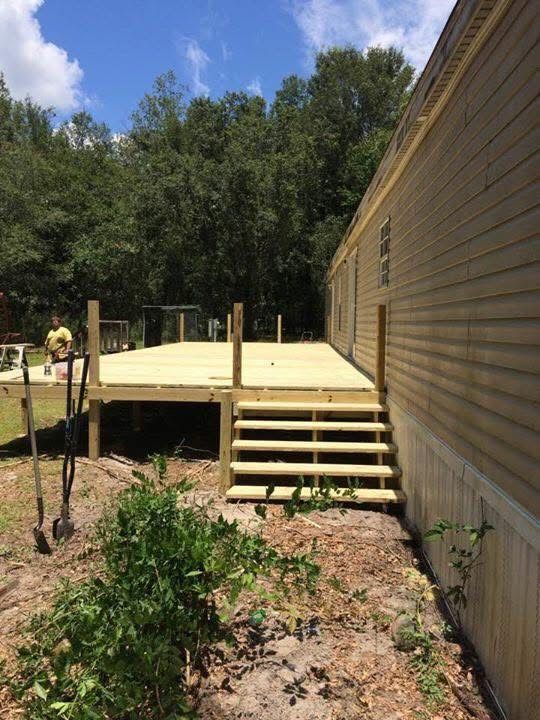 Wooden deck under construction beside a tan house, with steps and trees in the background.