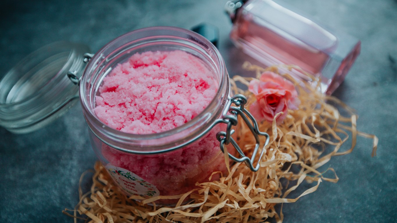 A jar filled with pink sugar next to a bottle of perfume.